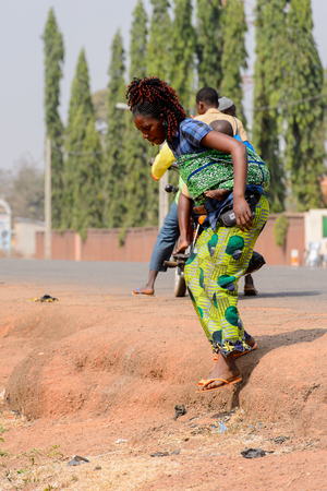 BOHICON, BENIN - JAN 12, 2017: Unidentified Beninese curly woman carries a baby on her back at the local market. Benin people suffer of poverty due to the bad economy.のeditorial素材