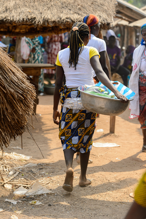 BOHICON, BENIN - JAN 12, 2017: Unidentified Beninese woman with braids carries a basin at the local market. Benin people suffer of poverty due to the bad economy.のeditorial素材