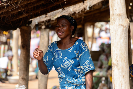 BOHICON, BENIN - JAN 12, 2017: Unidentified Beninese woman in blue and white shirt opens her mouth at the local market. Benin people suffer of poverty due to the bad economy.のeditorial素材