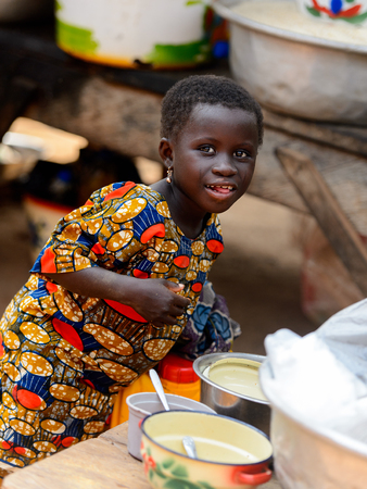BOHICON, BENIN - JAN 12, 2017: Unidentified Beninese little girl in colored dress stands behind the table at the local market. Benin children suffer of poverty due to the bad economy.のeditorial素材