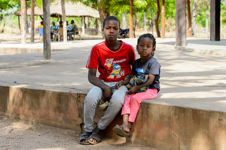 KOUTAMMAKOU, TOGO - JAN 13, 2017: Unidentified Togolese boy in red shirt hugs his little sister in the village. Togo children suffer of poverty due to the bad economy.のeditorial素材