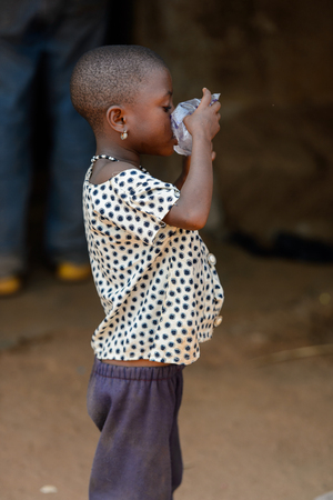 BOHICON, BENIN - JAN 12, 2017: Unidentified Beninese little girl drinks water from plastic bag at the local market. Benin children suffer of poverty due to the bad economy.のeditorial素材