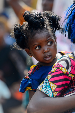 BOHICON, BENIN - JAN 12, 2017: Unidentified Beninese woman with braids carries a baby girl on her back at the local market. Benin people suffer of poverty due to the bad economy.のeditorial素材