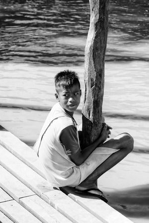 INLE LAKE, MYANMAR - AUG 30, 2016: Unidentified Burmese boy sits on a pier. 68 per cent of Myanma people belong to Bamar ethnic groupのeditorial素材