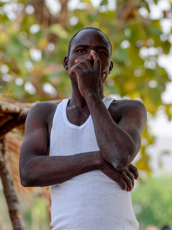 KOUTAMMAKOU, TOGO - JAN 13, 2017: Unidentified Togolese man in white shirt and red shorts stands in the village. Togo people suffer of poverty due to the bad economy.のeditorial素材