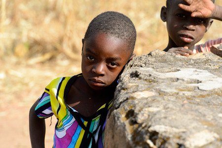 KOUTAMMAKOU, TOGO - JAN 13, 2017: Unidentified Togolese little girl in colored shirt stands behind the rock in the village. Togo children suffer of poverty due to the bad economy.のeditorial素材