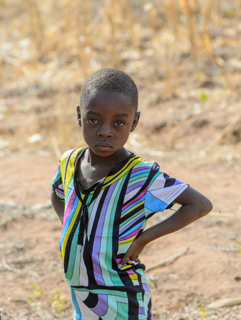 KOUTAMMAKOU, TOGO - JAN 13, 2017: Unidentified Togolese little girl in colored shirt stands in the village. Togo children suffer of poverty due to the bad economy.のeditorial素材