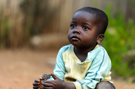 MASSIF KABYE, TOGO - JAN 13, 2017: Unidentified Togolese  little girl in colored shirt squats in the village. Togo children suffer of poverty due to the bad economy.のeditorial素材