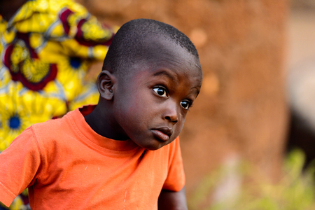 MASSIF KABYE, TOGO - JAN 13, 2017: Unidentified Togolese little boy in orange shirt looks ahead in the village. Togo children suffer of poverty due to the bad economy.のeditorial素材