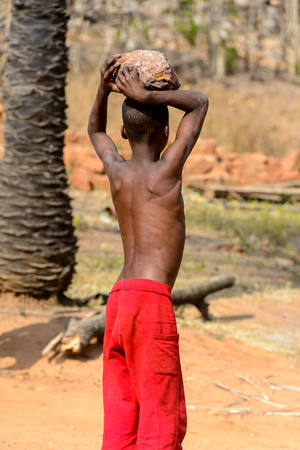 KARA REG., TOGO - JAN 14, 2017: Unidentified Konkomba boy in red shorts holds a rock in the village. Konkombas are ethnic group of Togoのeditorial素材