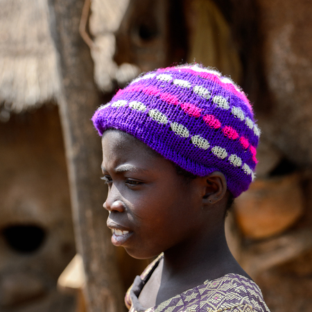 KARA REG., TOGO - JAN 14, 2017: Unidentified Konkomba little girl in colored hat looks ahead in the village. Konkombas are ethnic group of Togoのeditorial素材
