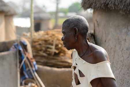 GHANI, GHANA - JAN 14, 2017: Unidentified Ghanaian old woman in white holey shirt looks ahead in the Ghani village. Ghana people suffer of poverty due to the bad economy.のeditorial素材