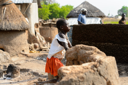 GHANI, GHANA - JAN 14, 2017: Unidentified Ghanaian little girl in white shirt and orange skirt walks in the Ghani village. Ghana children suffer of poverty due to the bad economy.のeditorial素材