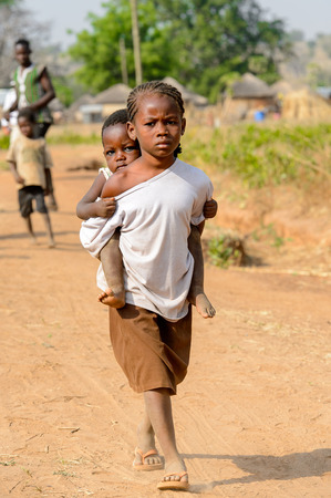 GHANI, GHANA - JAN 14, 2017: Unidentified Ghanaian little girl carries a baby on her back in the Ghani village. Ghana children suffer of poverty due to the bad economy.のeditorial素材