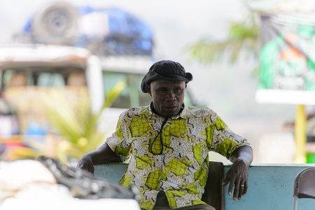 BRONG AHAFO, GHANA - JAN 15, 2017: Unidentified Ghanaian man in colored shirt and a hat sits on the chair. Ghana people suffer of poverty due to the bad economy.のeditorial素材