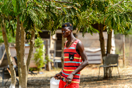 BRONG AHAFO, GHANA - JAN 15, 2017: Unidentified Ghanaian man in striped shirt and red panrs carries a bucket. Ghana people suffer of poverty due to the bad economy.のeditorial素材