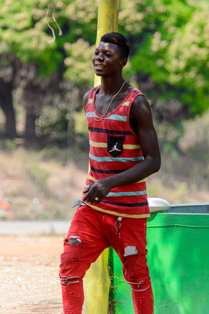 BRONG AHAFO, GHANA - JAN 15, 2017: Unidentified Ghanaian man in striped shirt and red pants walks on the street. Ghana people suffer of poverty due to the bad economy.のeditorial素材