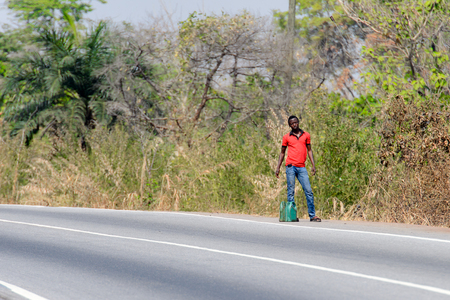 BRONG AHAFO, GHANA - JAN 15, 2017: Unidentified Ghanaian man in red shirt stands beside the road. Ghana people suffer of poverty due to the bad economy.のeditorial素材