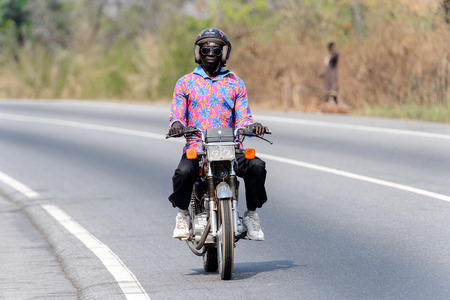 BRONG AHAFO, GHANA - JAN 15, 2017: Unidentified Ghanaian man in colored shirt and a helmet rides a motorcycle. Ghana people suffer of poverty due to the bad economy.のeditorial素材