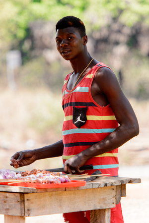 BRONG AHAFO, GHANA - JAN 15, 2017: Unidentified Ghanaian man in striped shirt cuts meat. Ghana people suffer of poverty due to the bad economy.のeditorial素材
