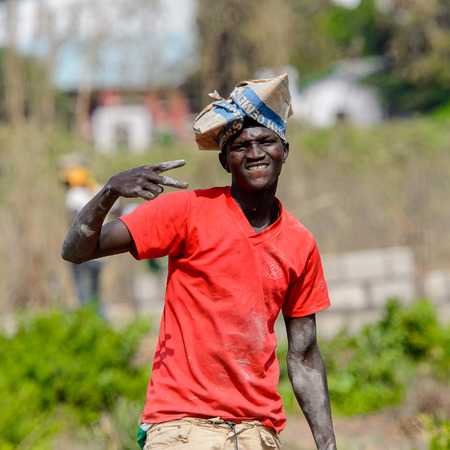 BRONG AHAFO, GHANA - JAN 15, 2017: Unidentified Ghanaian man in red shirt and paper bag on his head smiles. Ghana people suffer of poverty due to the bad economy.のeditorial素材