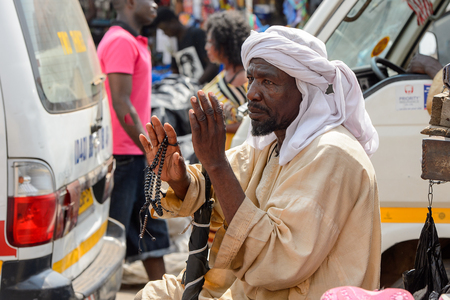 KUMASI, GHANA - JAN 15, 2017: Unidentified Ghanaian man in national clothes holds beads in his hand at the Kumasi market. Ghana people suffer of poverty due to the bad economy.のeditorial素材