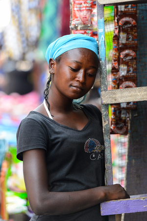 KUMASI, GHANA - JAN 15, 2017: Unidentified Ghanaian woman in blue headscarf looks down at the Kumasi market. Ghana people suffer of poverty due to the bad economy.のeditorial素材