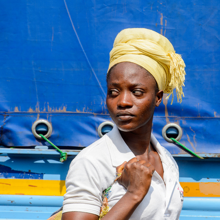 KUMASI, GHANA - JAN 15, 2017: Unidentified Ghanaian woman in white shirt and yellow headscarf walks...