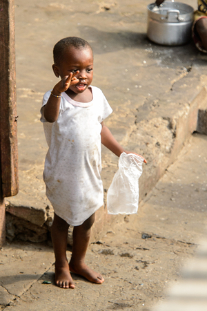 ACCRA, GHANA - JAN 8, 2017: Unidentified Ghanaian little girl in white dress holds a plastic bag. Children of Ghana suffer of poverty due to the economic situationのeditorial素材