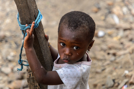 ACCRA, GHANA - JAN 8, 2017: Unidentified Ghanaian little girl in dirty white shirt holds on the...