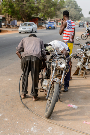 ACCRA, GHANA - JAN 8, 2017: Unidentified Ghanaian two men stand near the motocycle on the street. People of Ghana suffer of poverty due to the economic situationのeditorial素材