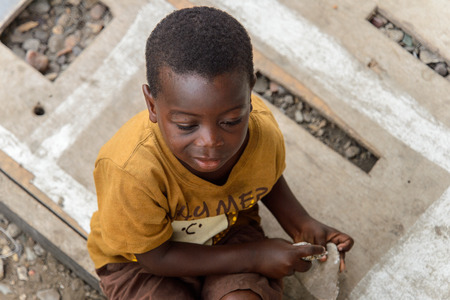 ACCRA, GHANA - JAN 8, 2017: Unidentified Ghanaian little boy in mustard shirt holds a couple of rocks in his hands. Children of Ghana suffer of poverty due to the economic situationのeditorial素材