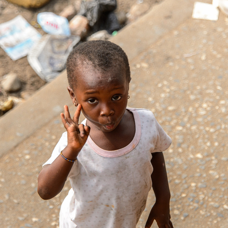 ACCRA, GHANA - JAN 8, 2017: Unidentified Ghanaian little girl in dirty white dress shows her fingers on the street. Children of Ghana suffer of poverty due to the economic situationのeditorial素材
