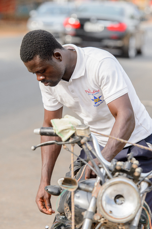 ACCRA, GHANA - JAN 8, 2017: Unidentified Ghanaian man stand near the motocycle on the street. People of Ghana suffer of poverty due to the economic situationのeditorial素材