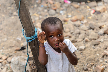 ACCRA, GHANA - JAN 8, 2017: Unidentified Ghanaian little girl tries to put her fingers into the mouth near the wooden pole. Children of Ghana suffer of poverty due to the economic situationのeditorial素材