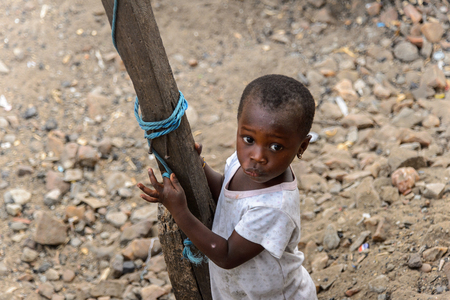 ACCRA, GHANA - JAN 8, 2017: Unidentified Ghanaian little girl in dirty white shirt holds on the wooden pole. Children of Ghana suffer of poverty due to the economic situationのeditorial素材