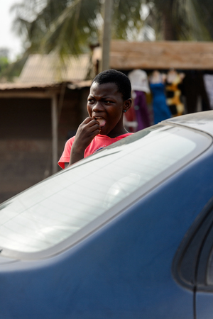 ACCRA, GHANA - JAN 8, 2017: Unidentified Ghanaian girl puts something into her mouth behind the car. People of Ghana suffer of poverty due to the economic situationのeditorial素材