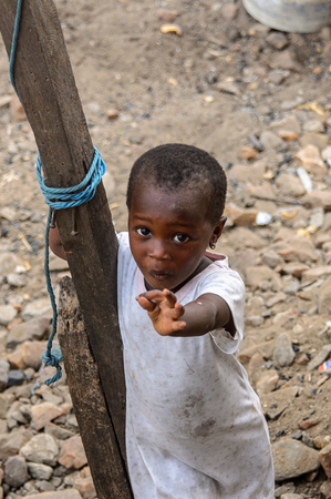 ACCRA, GHANA - JAN 8, 2017: Unidentified Ghanaian little girl in dirty white dress holds on the wooden pole. Children of Ghana suffer of poverty due to the economic situationのeditorial素材