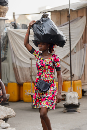 LOME, TOGO - Jan 9, 2017: Unidentified Togolese woman carries a plastic bag on her head at the Lome central market. Togo people suffer of poverty due to the bad economyのeditorial素材