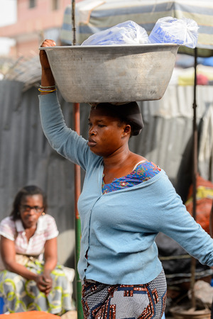 LOME, TOGO - Jan 9, 2017: Unidentified Togolese woman carries a basin on her head at the Lome central market. Togo people suffer of poverty due to the bad economyのeditorial素材