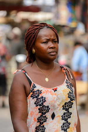 LOME, TOGO - Jan 9, 2017: Unidentified Togolese woman with braids in colored dress walk at the Lome central market. Togo people suffer of poverty due to the bad economyのeditorial素材
