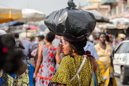 LOME, TOGO - Jan 9, 2017: Unidentified Togolese woman carries a plastic bag on her head at the Lome central market. Togo people suffer of poverty due to the bad economyのeditorial素材