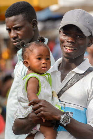 LOME, TOGO - Jan 9, 2017: Unidentified Togolese little baby girl carried by her father at the Lome central market. Togo children suffer of poverty due to the bad economyのeditorial素材