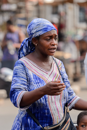 LOME, TOGO - Jan 9, 2017: Unidentified Togolese woman in blue dress and headscarf stands at the Lome central market. Togo people suffer of poverty due to the bad economyのeditorial素材