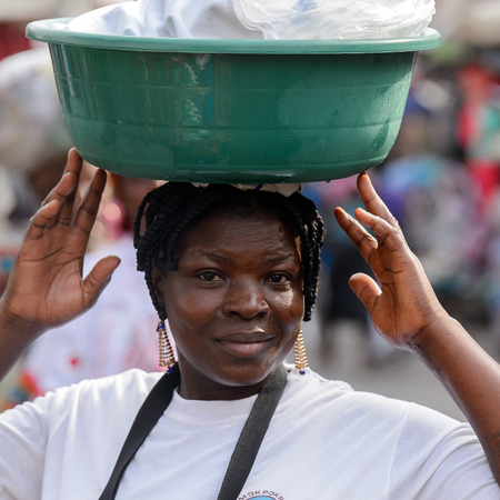 LOME, TOGO - Jan 9, 2017: Unidentified Togolese woman carries a basin on her head at the Lome central market. Togo people suffer of poverty due to the bad economyのeditorial素材