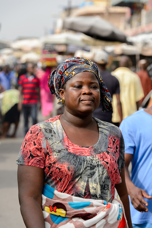 LOME, TOGO - Jan 9, 2017: Unidentified Togolese woman in colored dress and headscarf walks at the Lome central market. Togo people suffer of poverty due to the bad economyのeditorial素材