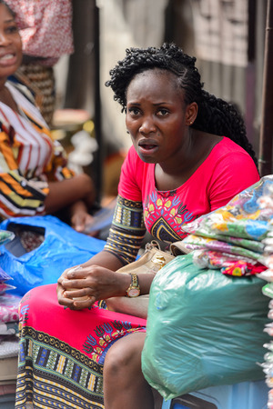 LOME, TOGO - Jan 9, 2017: Unidentified Togolese curly woman in red dress seats at the Lome central market. Togo people suffer of poverty due to the bad economyのeditorial素材