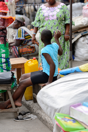 LOME, TOGO - Jan 9, 2017: Unidentified Togolese woman seats on the wooden bench at the Lome central market. Togo people suffer of poverty due to the bad economyのeditorial素材