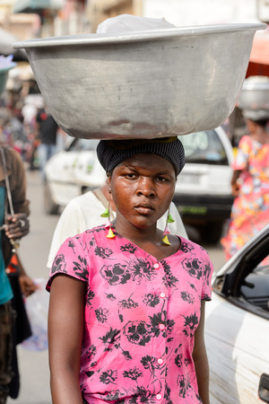 LOME, TOGO - Jan 9, 2017: Unidentified Togolese woman carries a basin on her head at the Lome central market. Togo people suffer of poverty due to the bad economyのeditorial素材