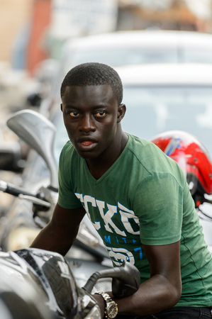 LOME, TOGO - Jan 9, 2017: Unidentified Togolese young man in green shirt stands near motocycles at the Lome central market. Togo people suffer of poverty due to the bad economyのeditorial素材